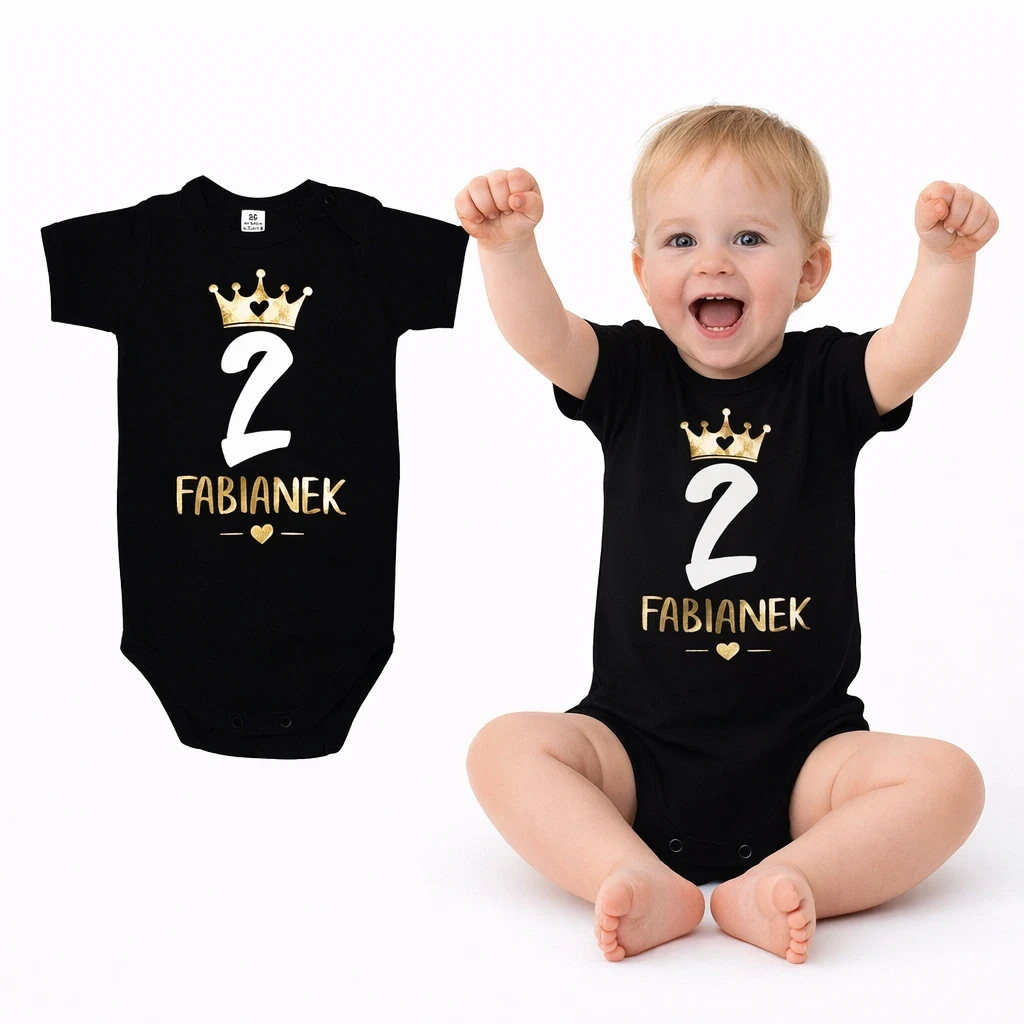 chłopiec w body dziecięcym koloru czarnego, z białą cyferką 2. Chłopiec unosi obie rączki do góry.